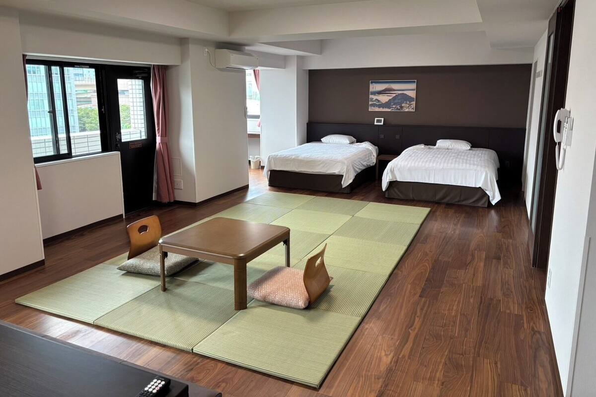 A hotel room with two beds, a small table, a chair, a TV, and a view of the outside.