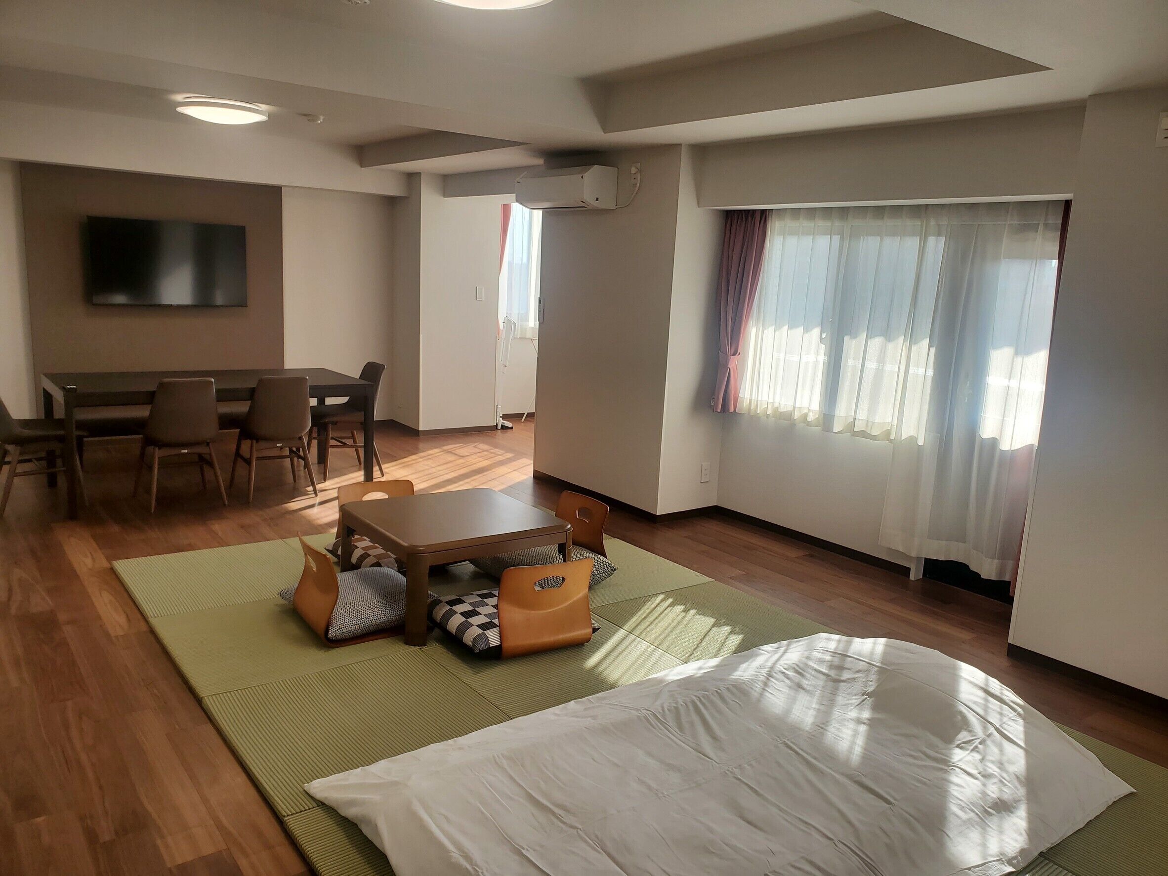 A room with a dining table, chairs, a sofa, a TV, and a window with curtains.