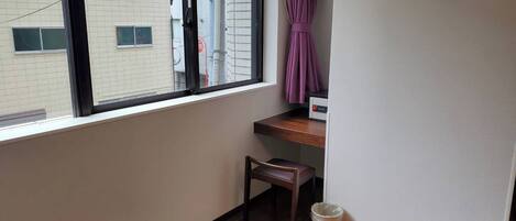 A small room with a wooden floor, a window with a black frame, a purple curtain, a small wooden chair, and a trash bin.