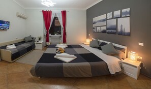 A modern bedroom with a large bed, a sofa, and a desk. There are multiple artworks on the wall and a TV on the wall. - Martini Rooms (Rome)