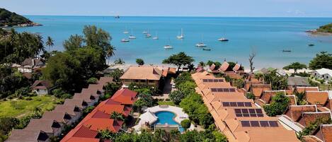 A coastal resort with multiple bungalow-style buildings, a swimming pool, and a view of the sea with boats.