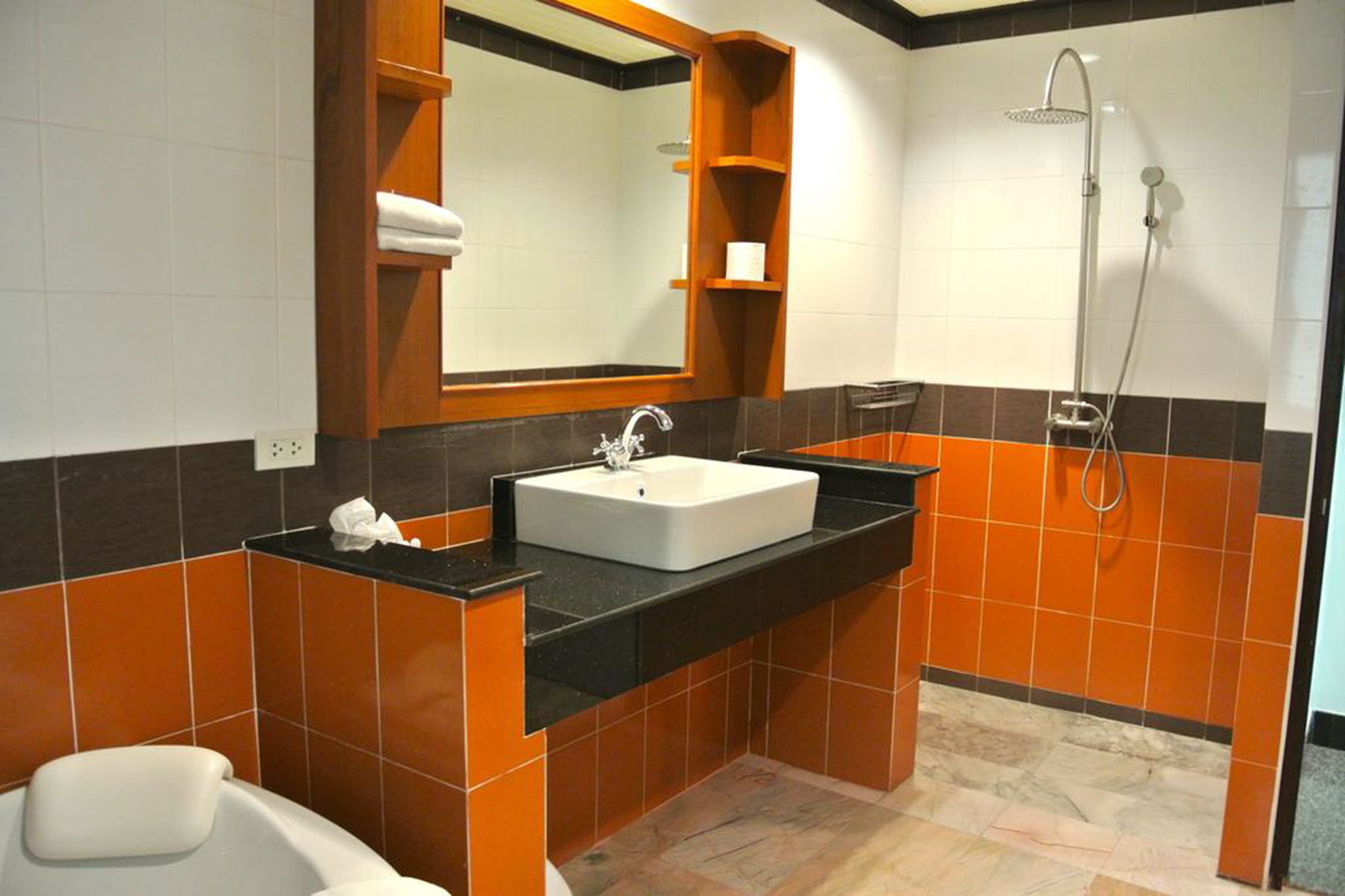 Ein Badezimmer mit einem weißen Waschbecken, einer schwarzen Arbeitsplatte, orangefarbenen und schwarzen Fliesen, einer weißen Badewanne und einer Dusche mit Duschbrause.