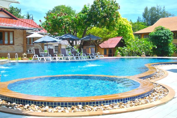 A swimming pool with lounge chairs and umbrellas, surrounded by trees and buildings. - PS Thana Resort (Koh Samui)