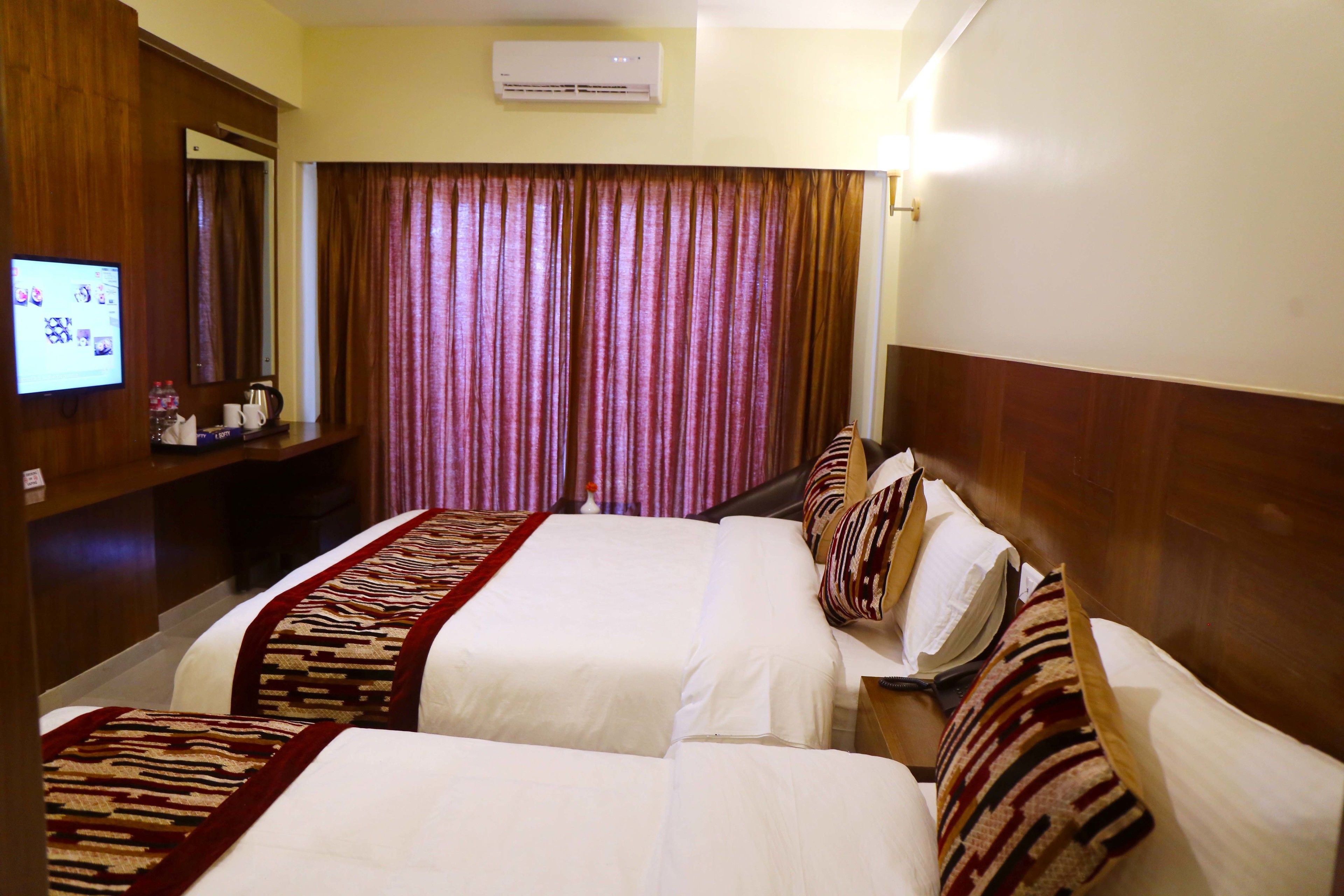 A hotel room with two beds, a TV, a mirror, and a curtain.