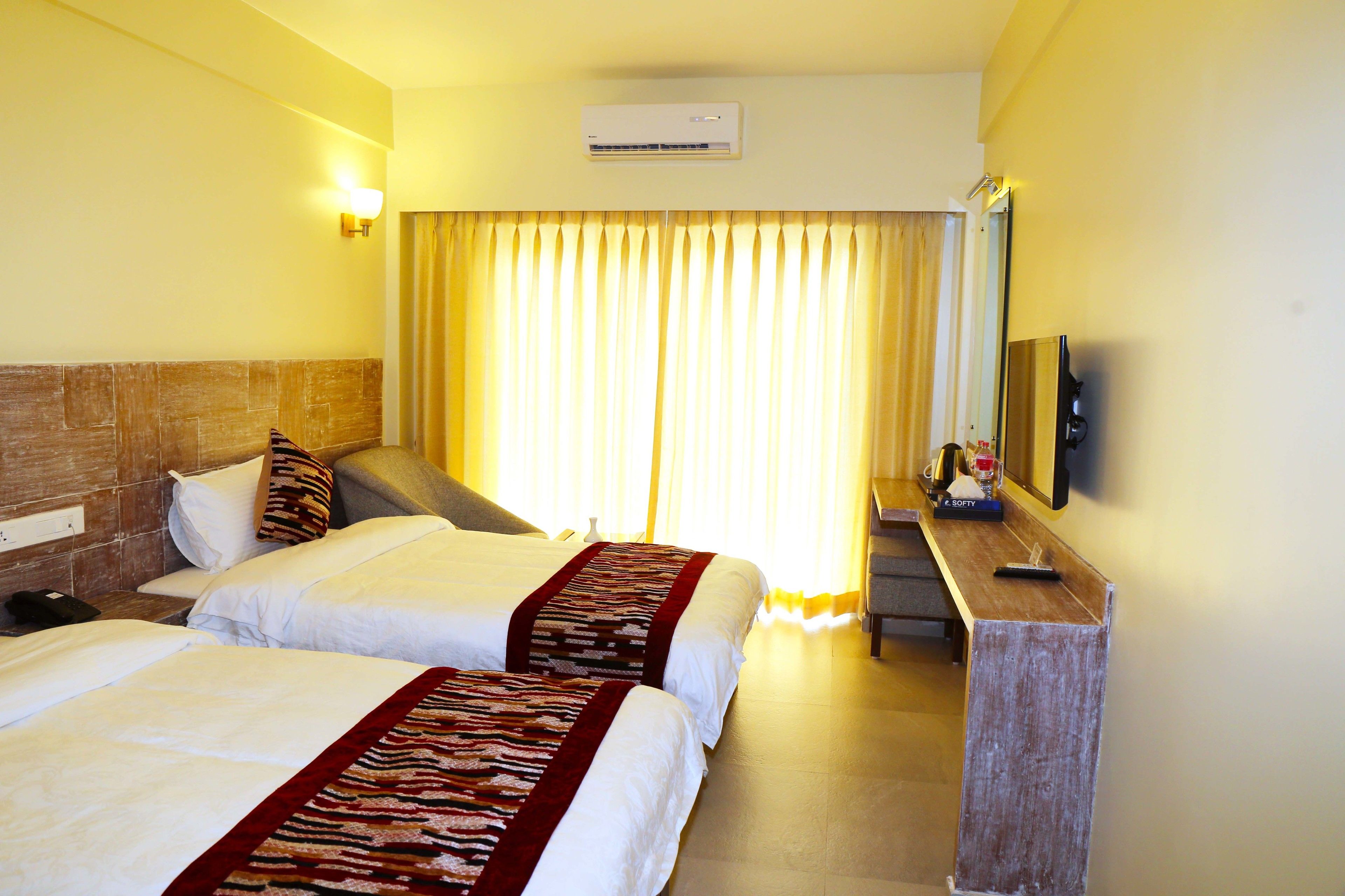 Habitación de hotel con dos camas, un escritorio, un espejo y un equipo de aire acondicionado.
