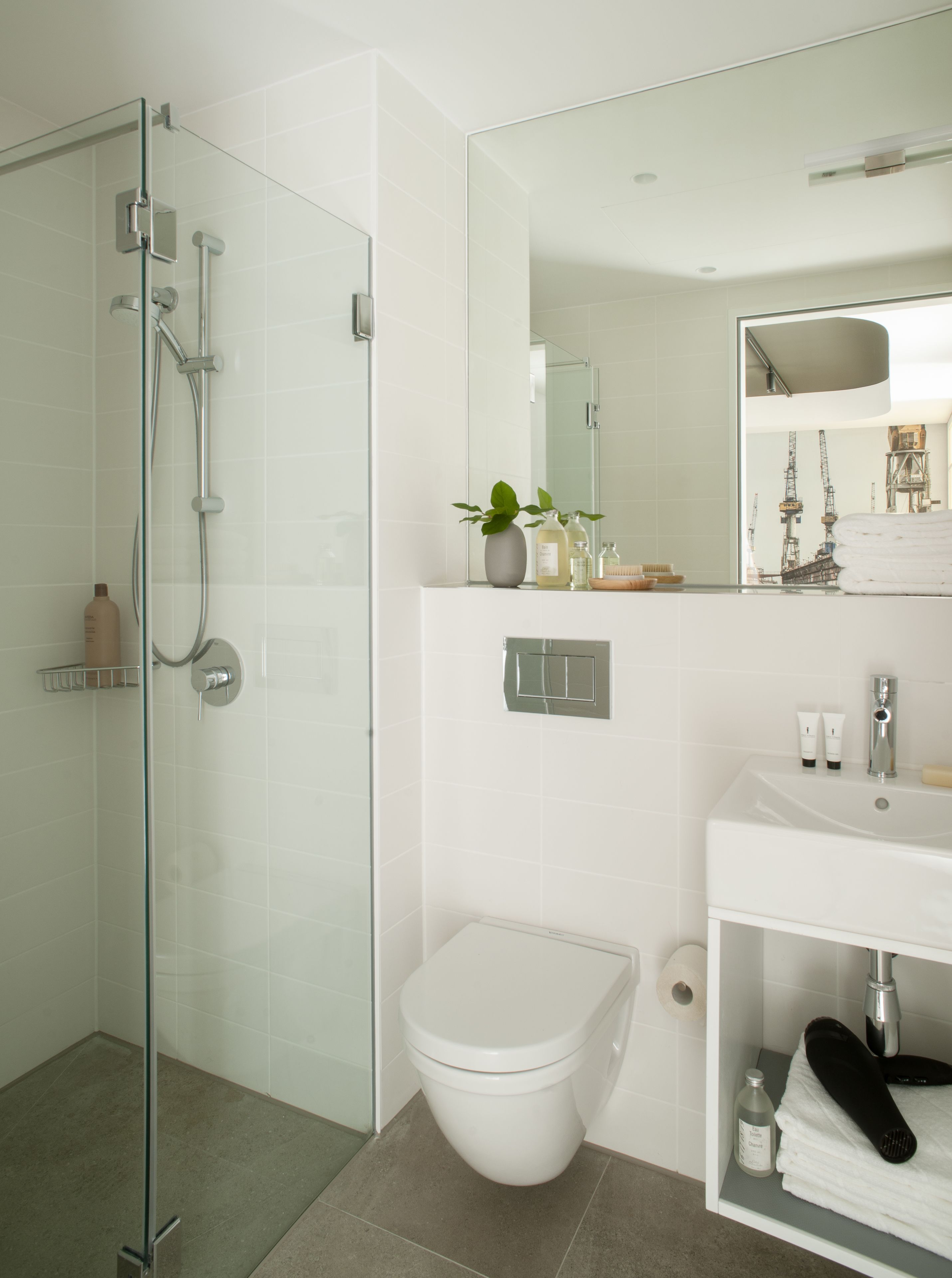 Un baño moderno con ducha de vidrio, inodoro blanco y tocador con espejo.