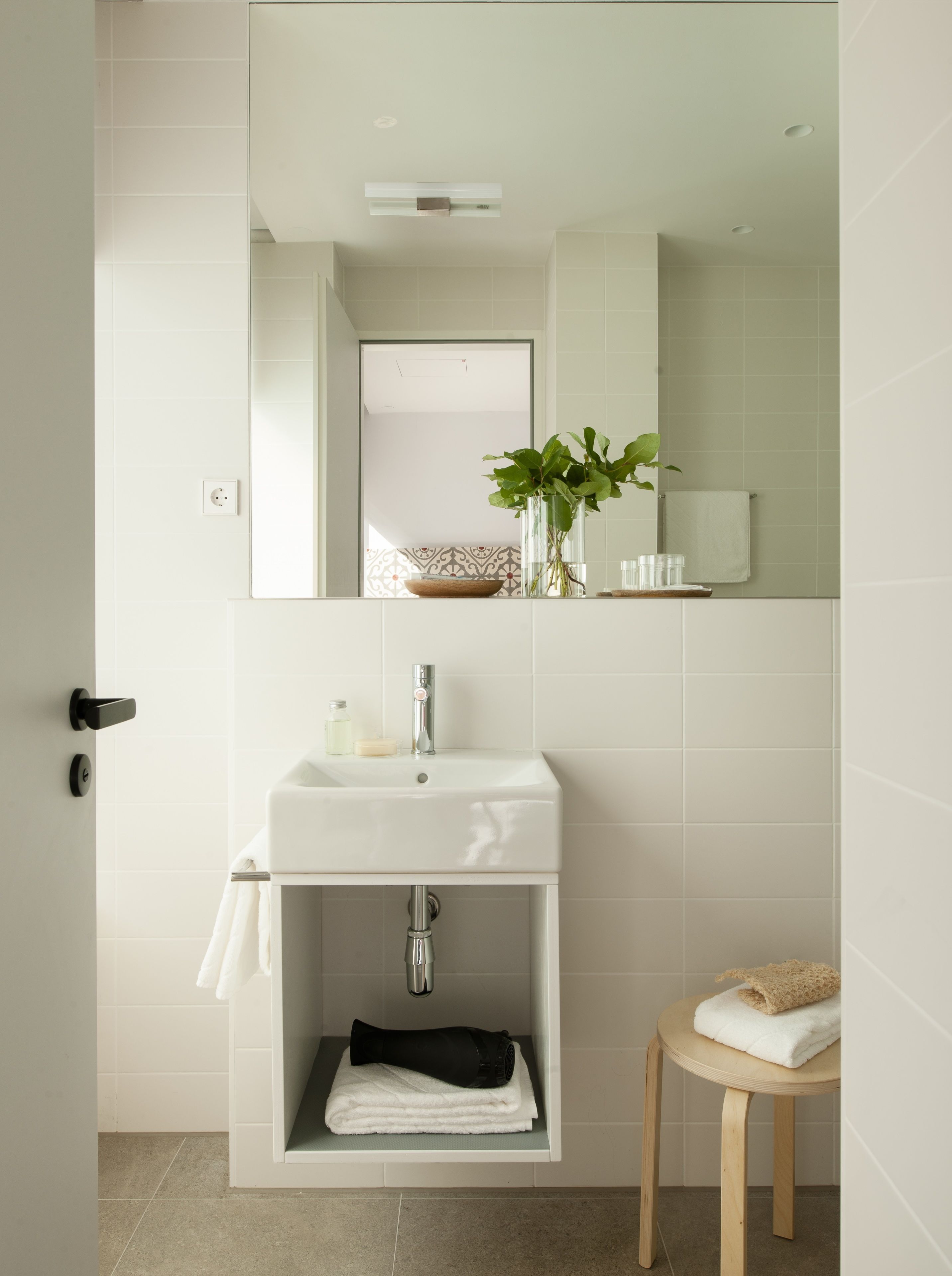 A modern bathroom with a white sink, mirror, and a small wooden stool.