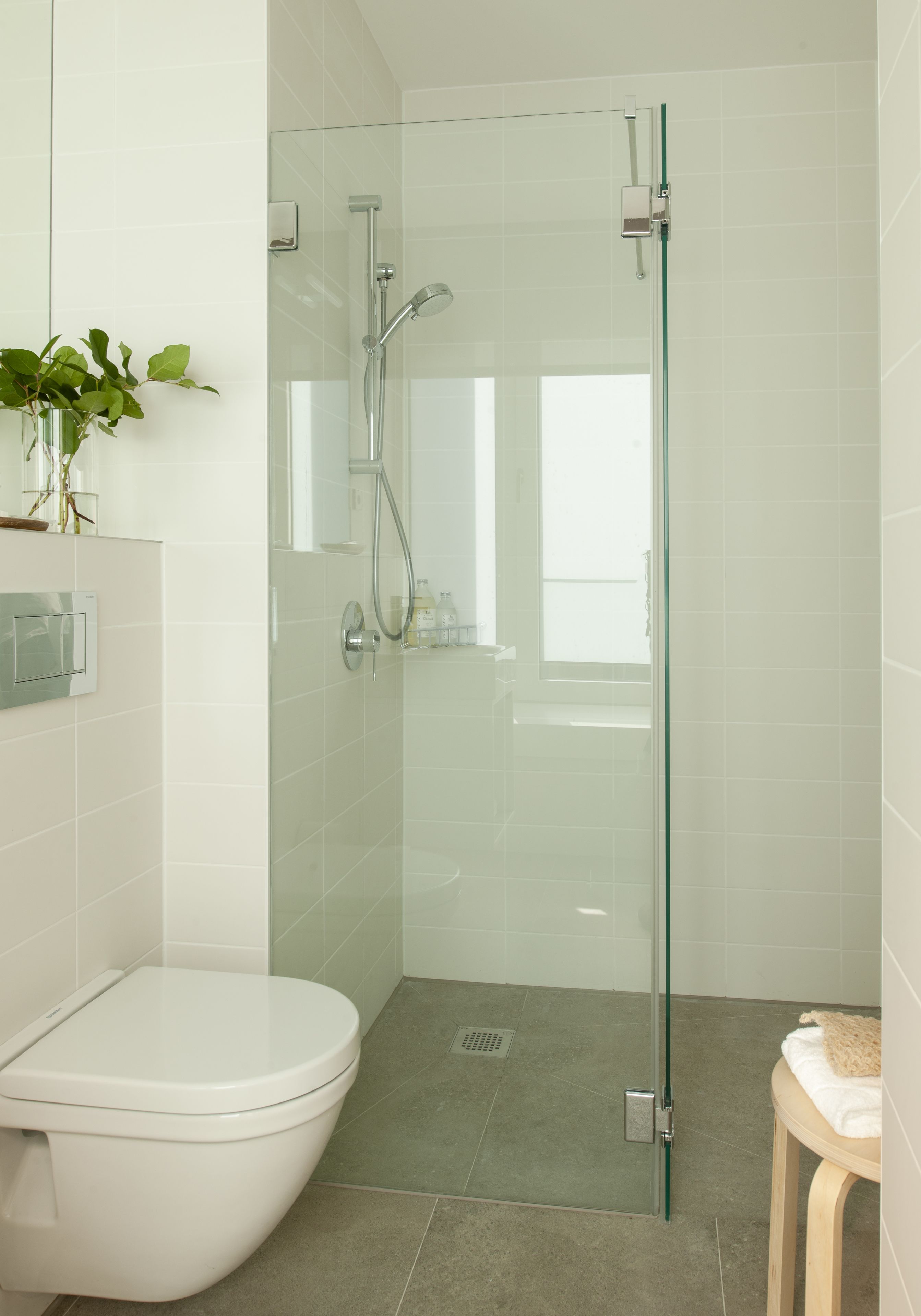 A modern bathroom with a glass-enclosed shower, a white toilet, and a small stool with a towel.