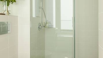 A modern bathroom with a glass-enclosed shower, a white toilet, and a small stool with a towel.