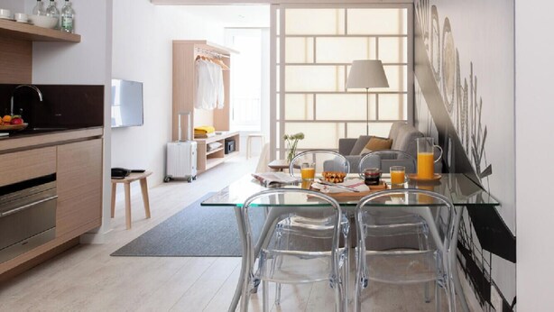 Una cocina moderna con una mesa de vidrio, sillas transparentes y vistas a un salón con sofá y lámpara.