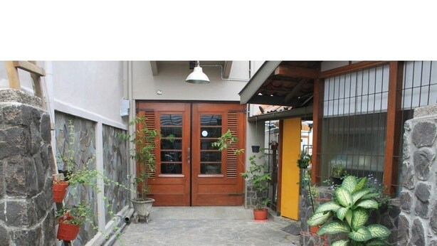 A stone-paved courtyard with a wooden door, potted plants, and a hanging light fixture. - De Riau Cottage by HouseinBandung (Bandung)