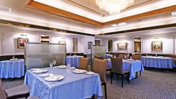 A hotel dining area with multiple tables set for dining, each with blue tablecloths and white plates.