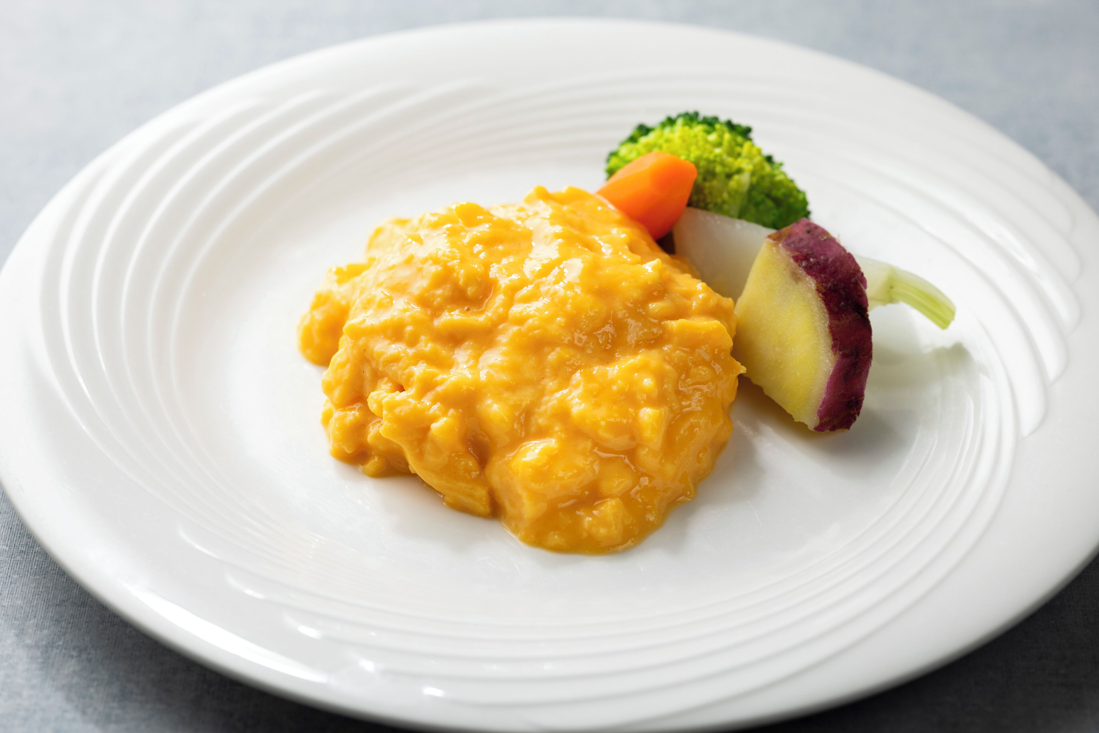 A white plate with a serving of macaroni and cheese, broccoli, and a slice of red potato.