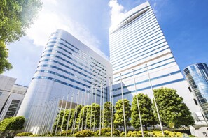 Un edificio moderno con fachada curva y varios pisos, rodeado de árboles y banderas.