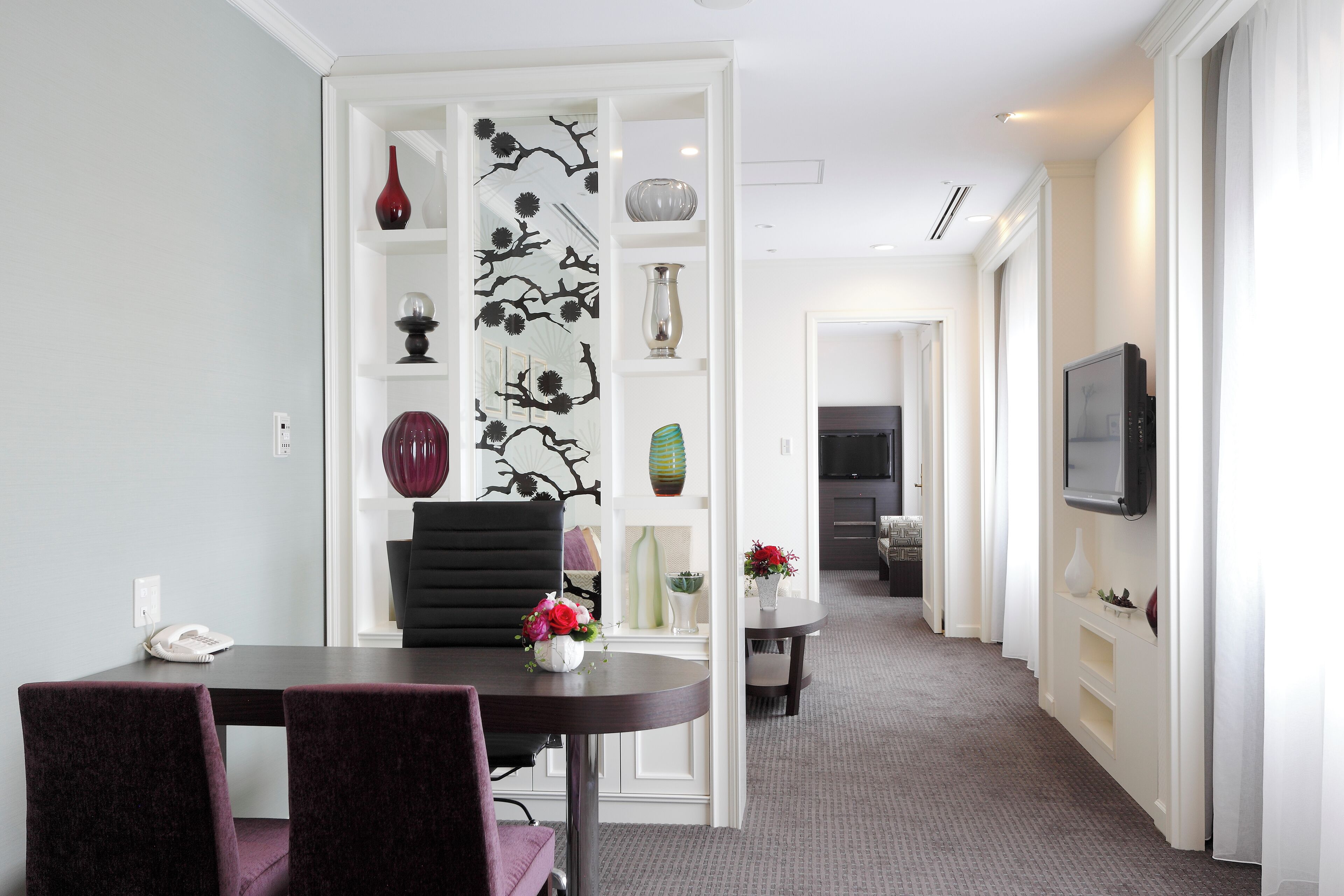 Een moderne eetruimte met een donkere tafel, paarse stoelen en een witte scheiding met decoratieve objecten.