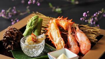 A seafood platter with shrimp, asparagus, and a pine cone on a dark background with purple flowers.