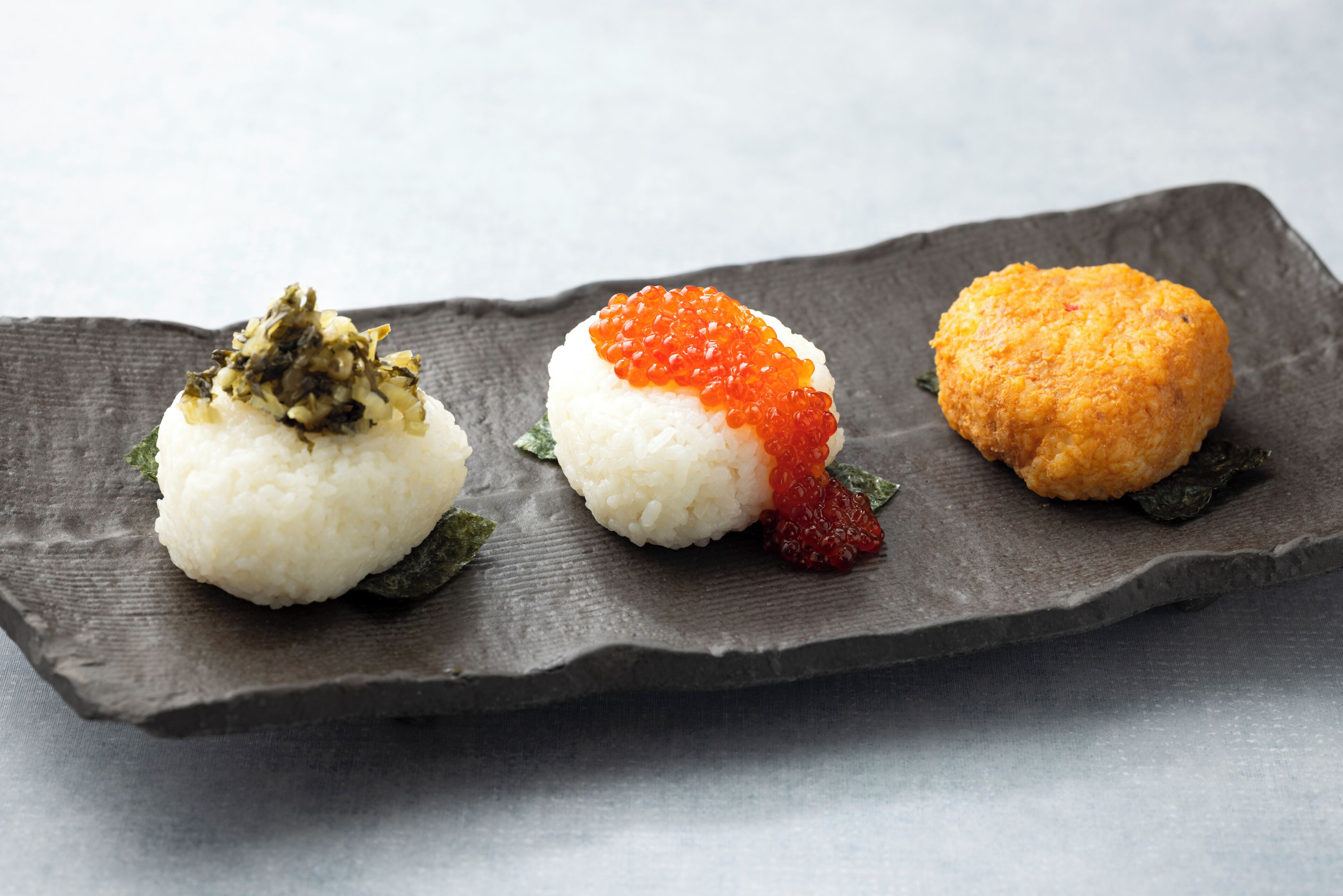 Three sushi pieces on a dark slate plate.
