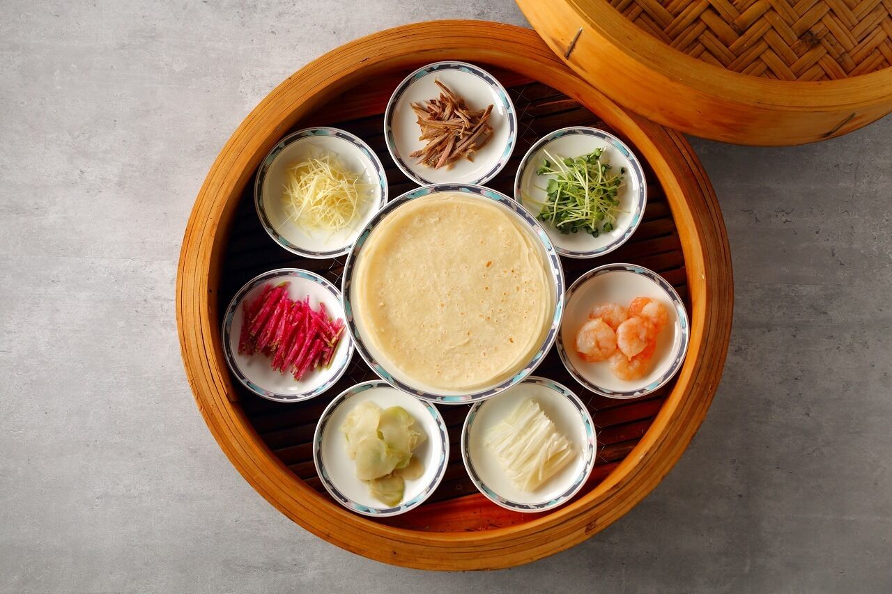 A round wooden tray with a central bowl of soup surrounded by smaller bowls containing various ingredients.