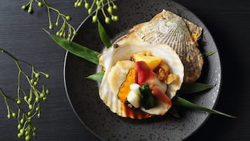 A plate with a scallop, mango, and vegetables on a dark plate.