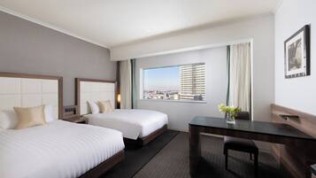 Habitación de hotel con dos camas, un escritorio y un amplio ventanal con vistas a la ciudad.