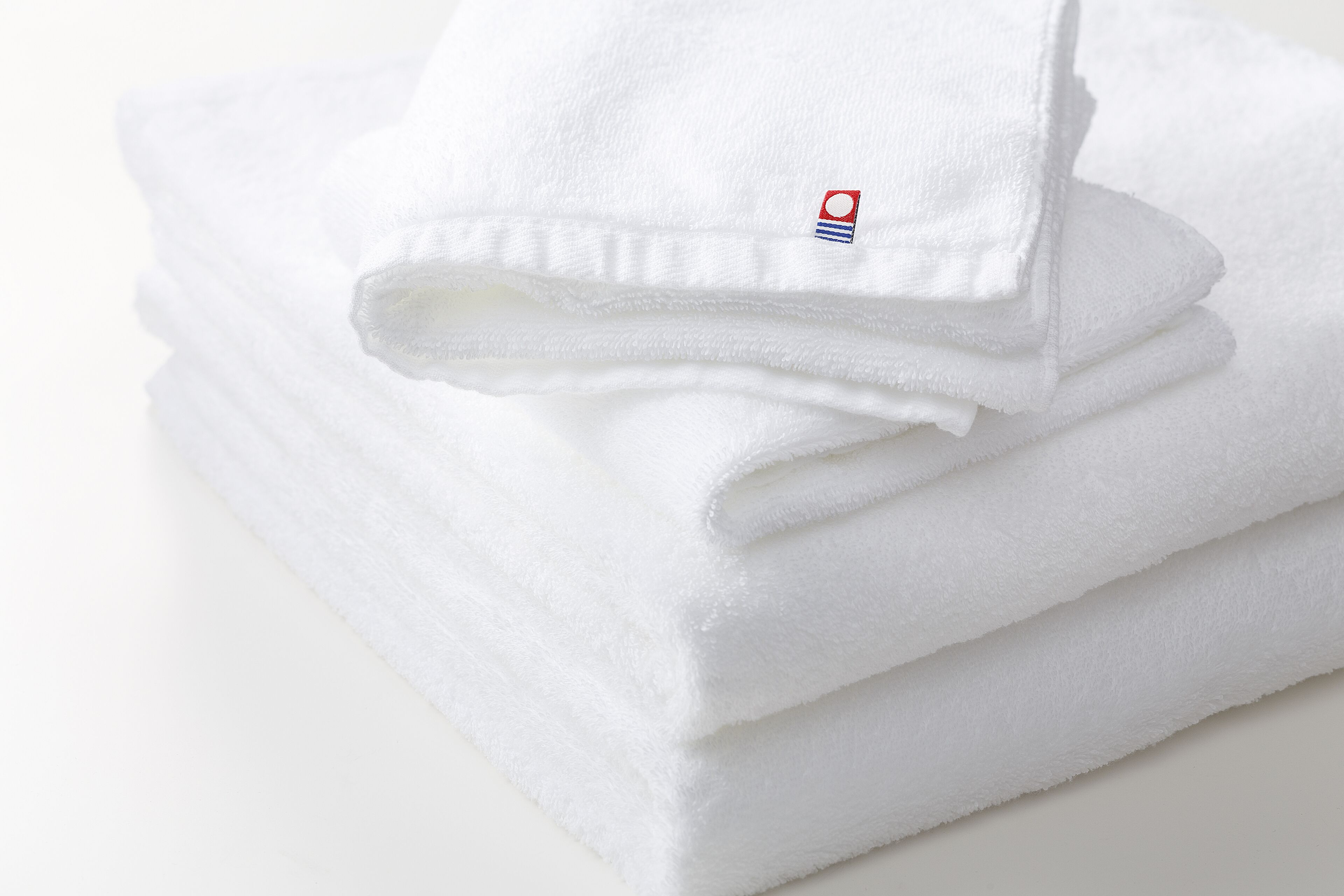 A stack of white towels with a small logo on the corner.