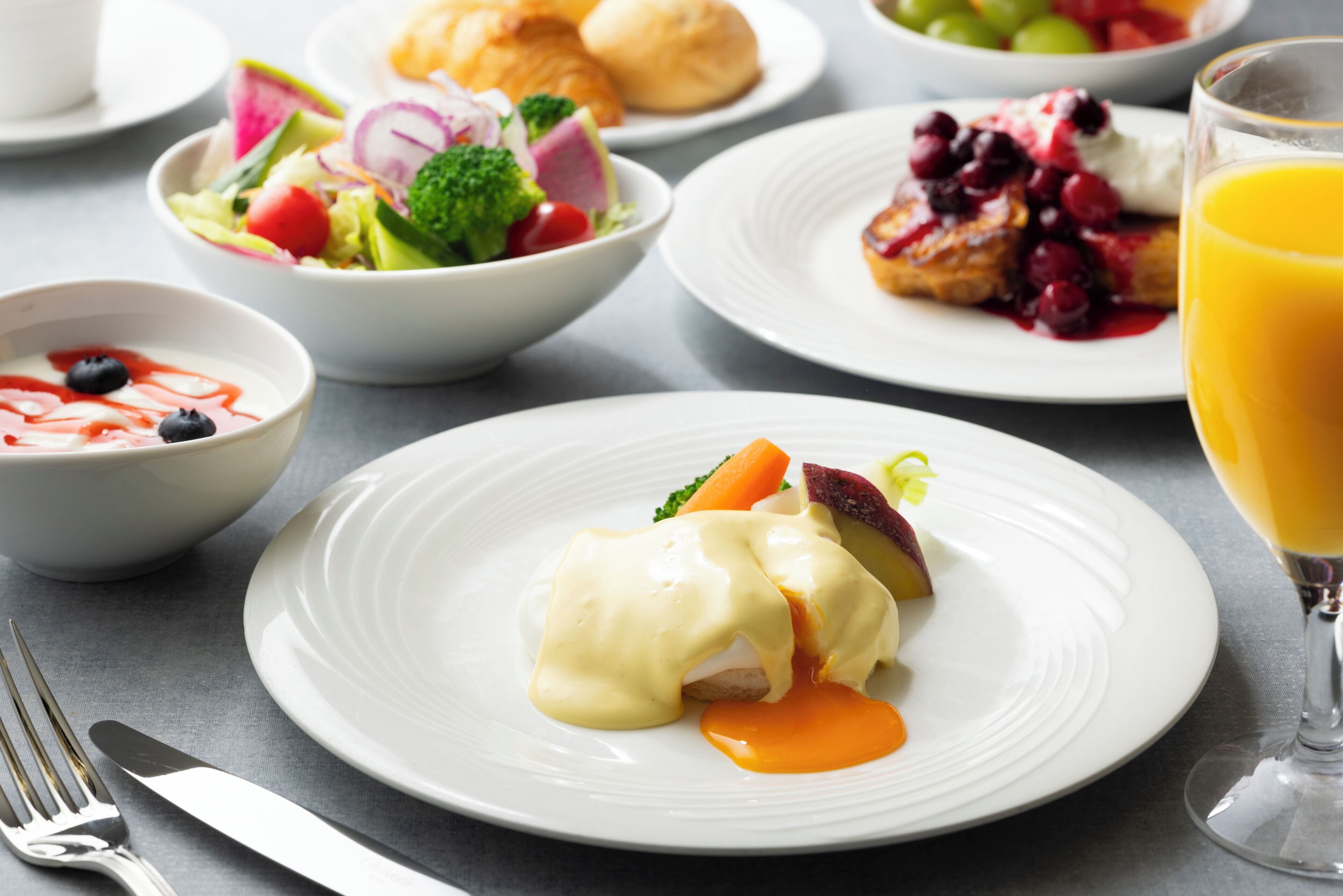 Ein Frühstückstisch mit verschiedenen Speisen, darunter Eggs Benedict, einem Obstsalat und einem Glas Orangensaft.