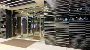 Entrada de um hotel com design moderno, destacando uma porta de vidro e uma placa com o texto "PALACE HOTEL OMIA".