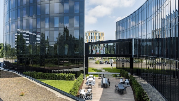 A modern building with curved glass facades and a courtyard with outdoor seating.