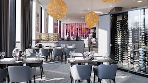 A modern restaurant interior with tables set for dining, a wine display, and a bar area.