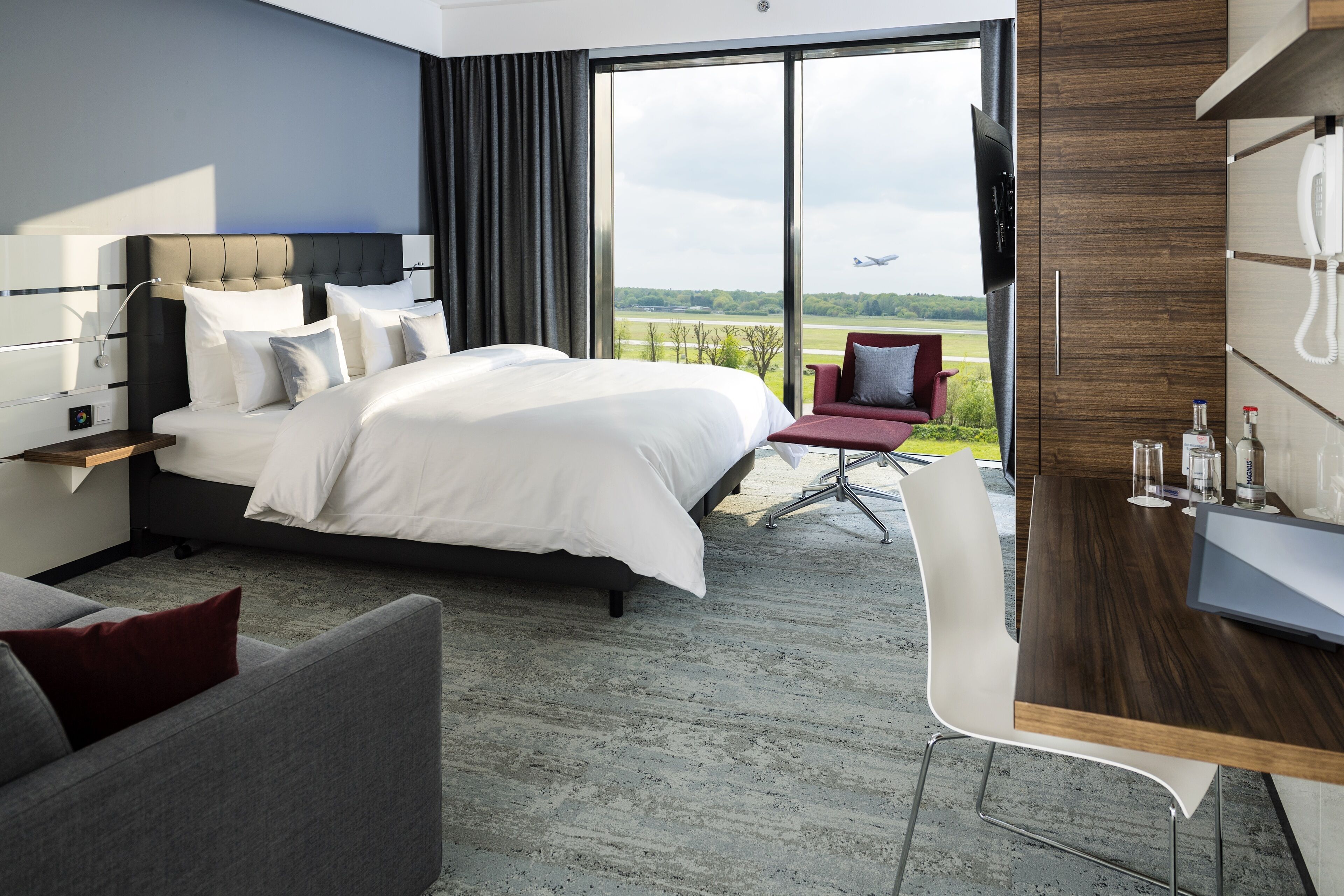 A modern hotel room with a large bed, a desk, and a view of the airport.