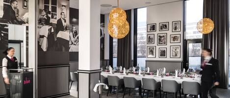 A modern dining area with a long table set for a meal, a reception desk, and framed photographs on the wall.