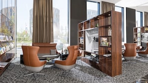 A modern library with leather chairs, bookshelves, and large windows offering city views.