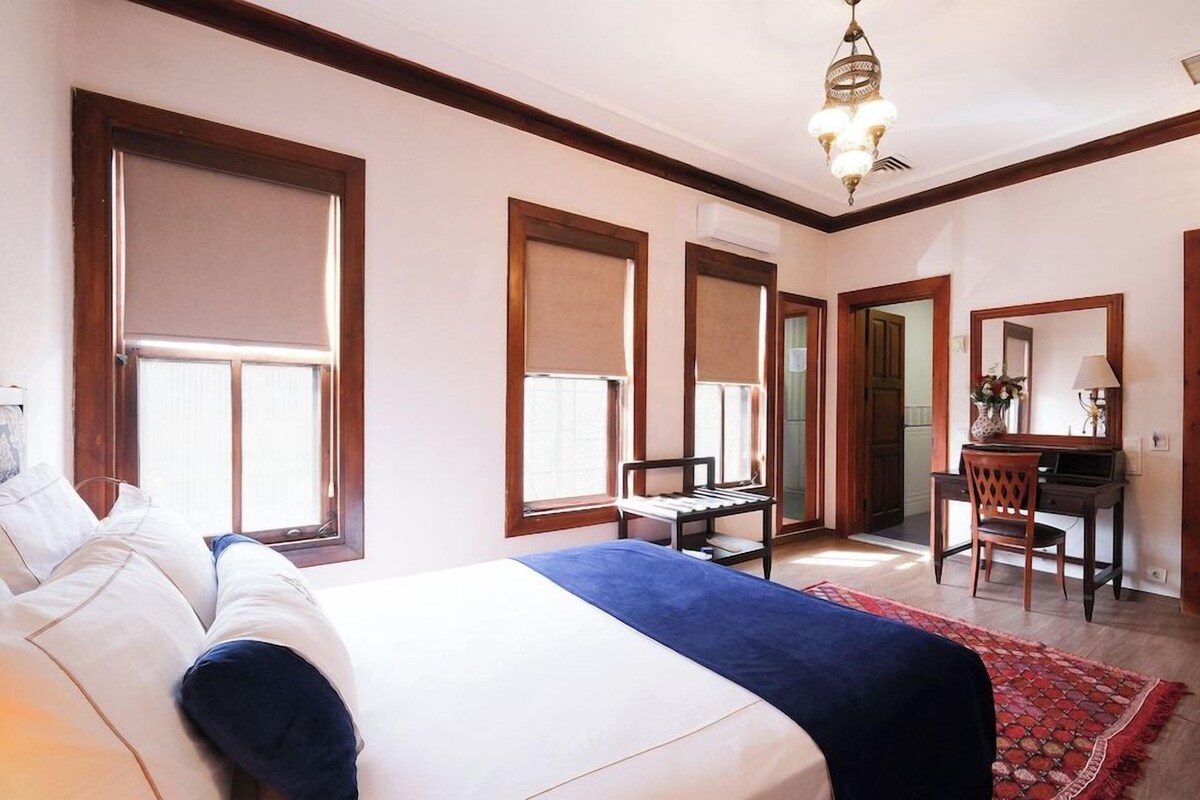 A bedroom with a bed, a desk, a chair, and a mirror.