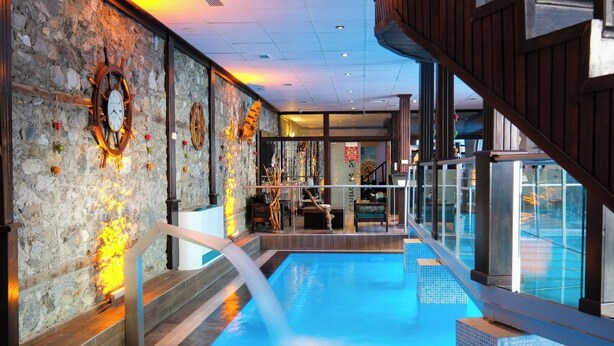 Ein Hallenbad mit Steinwänden und Holzelementen, einem Holzboden und Blick ins Freie.