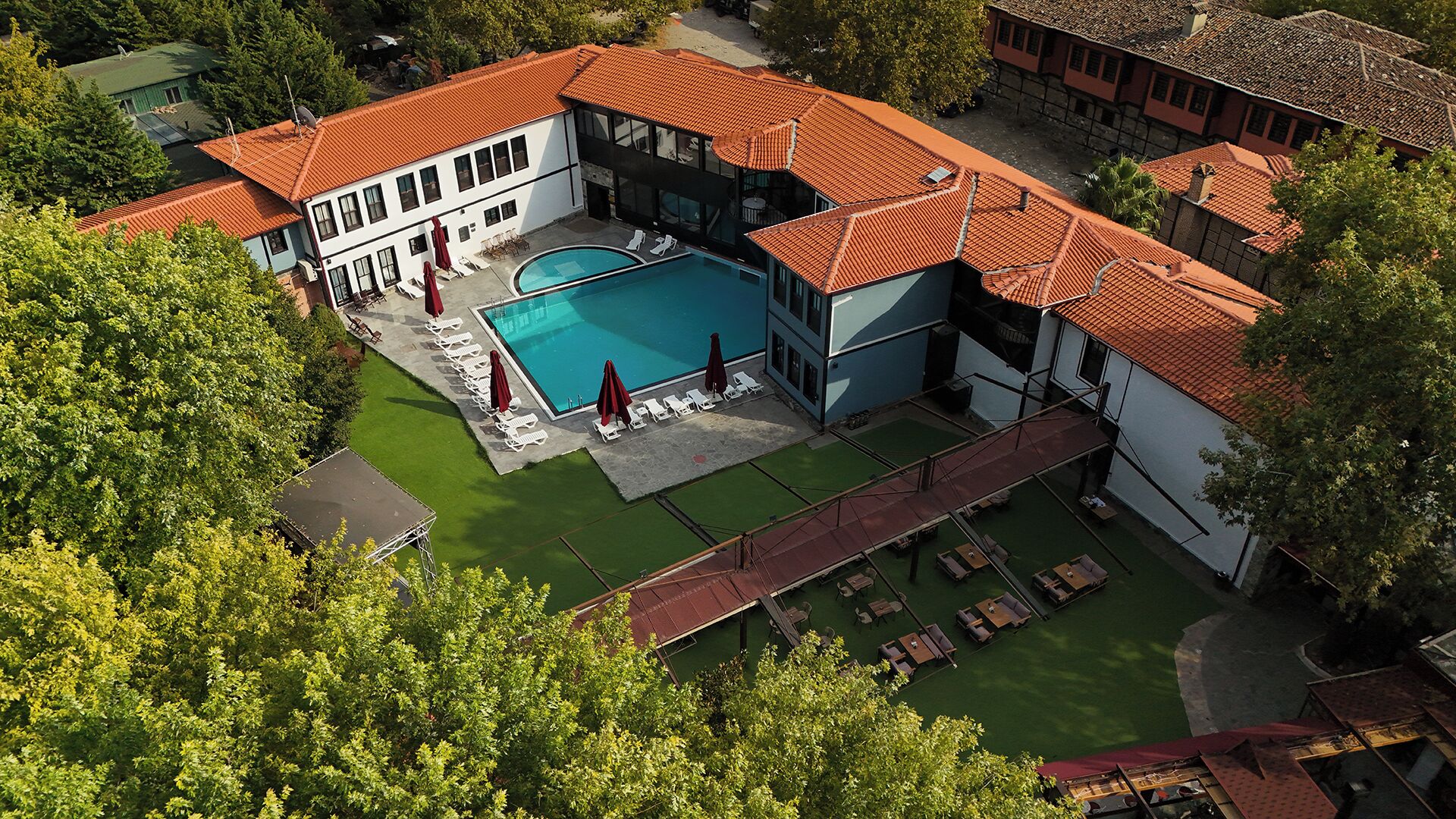 An aerial view of a resort with a swimming pool, sun loungers, and a covered outdoor seating area.