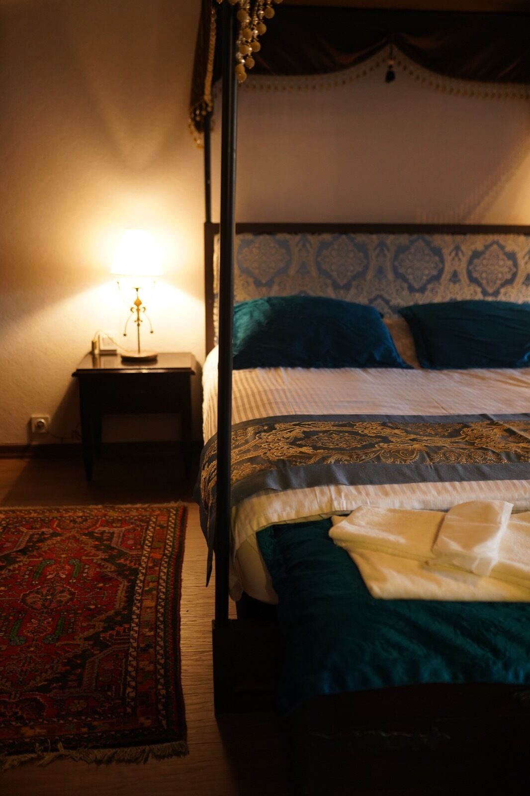 Una cama con una colcha estampada, una mesita de noche con una lámpara y una alfombra en el suelo.