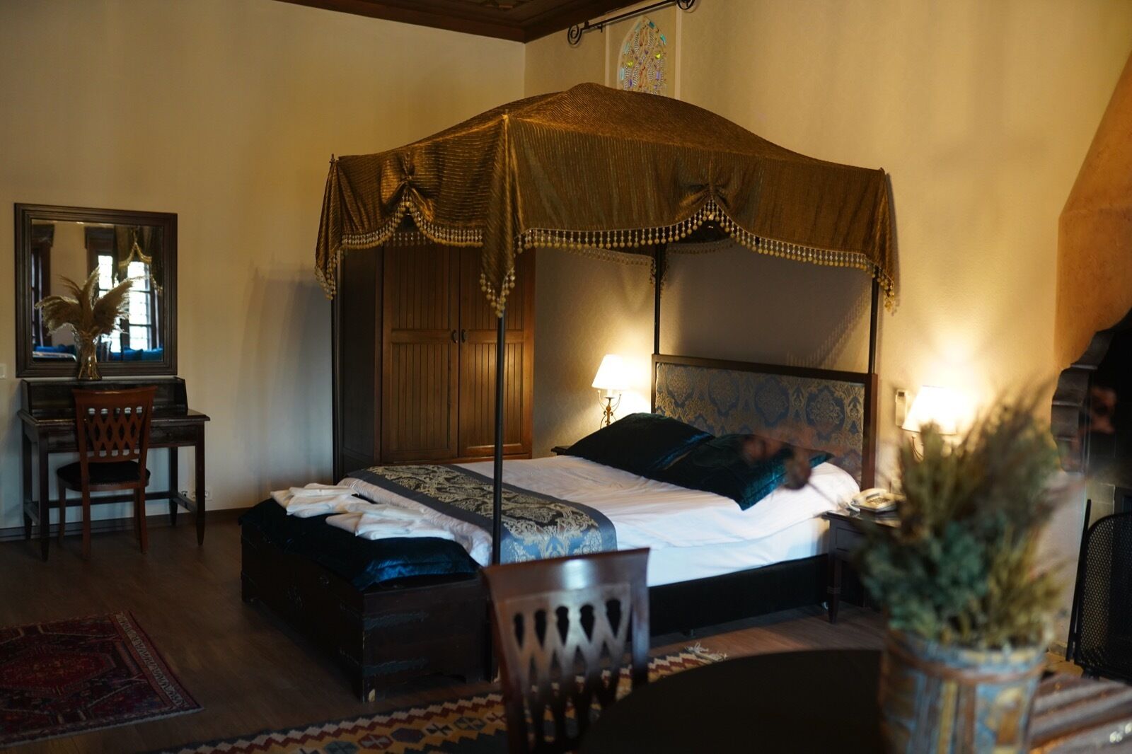 A four-poster canopy bed with a wooden headboard, a bedside table, and a chair.
