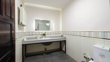Un baño con puerta de madera, un lavabo blanco con un espejo encima, una toalla colgada en la pared y un inodoro.