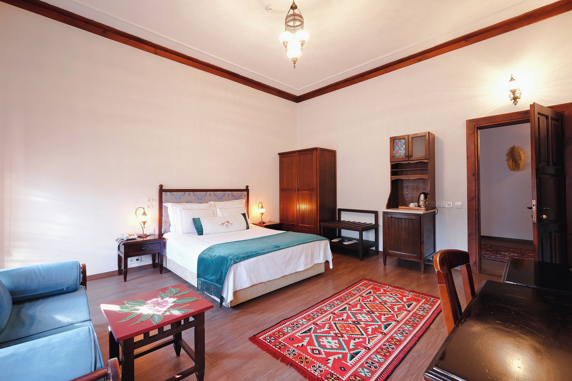Un dormitorio con una cama, un armario de madera, una mesita, una silla, un escritorio y una puerta.