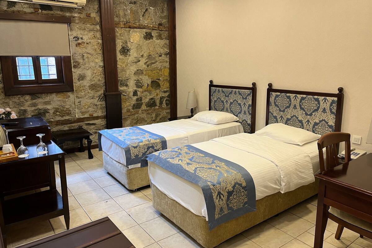 A room with two beds, a desk, a chair, and a stone wall.