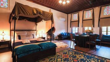 A four-poster bed with a canopy, a fireplace, a dining area with a table and chairs, and a patterned rug.