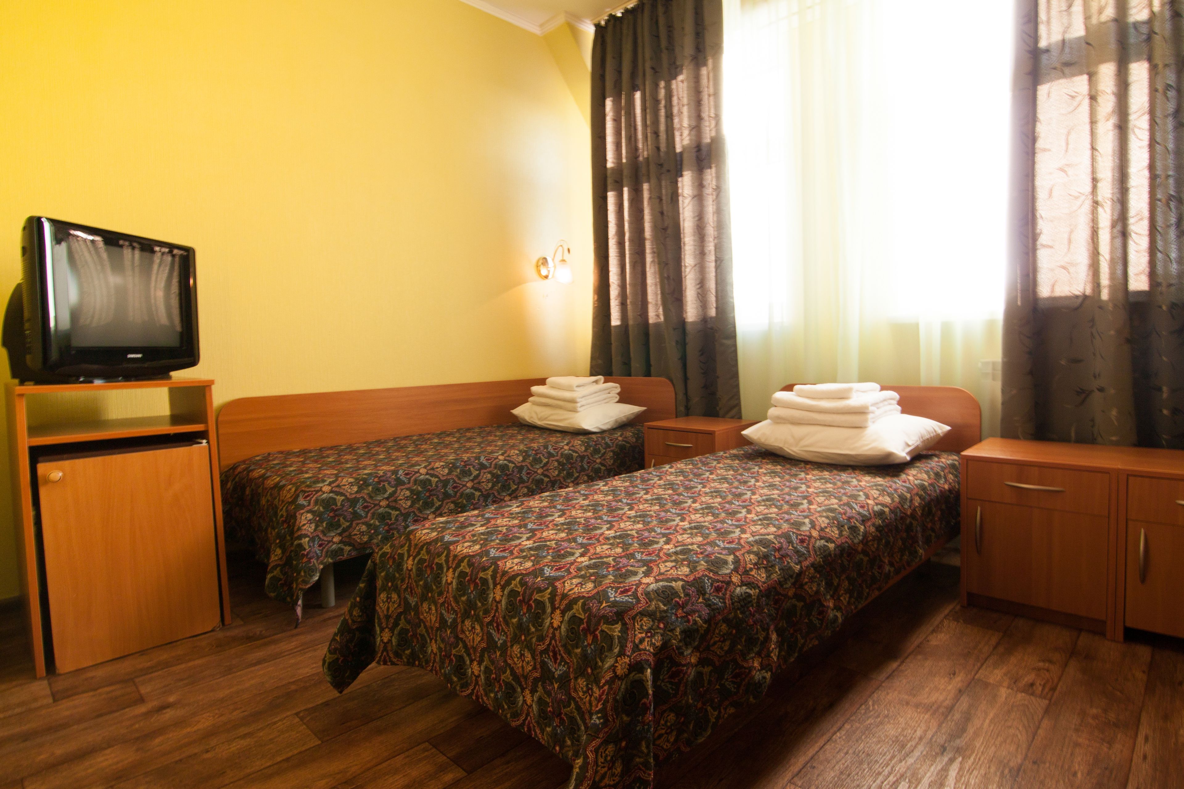 A hotel room with two single beds, a TV on a wooden stand, and a window with curtains.