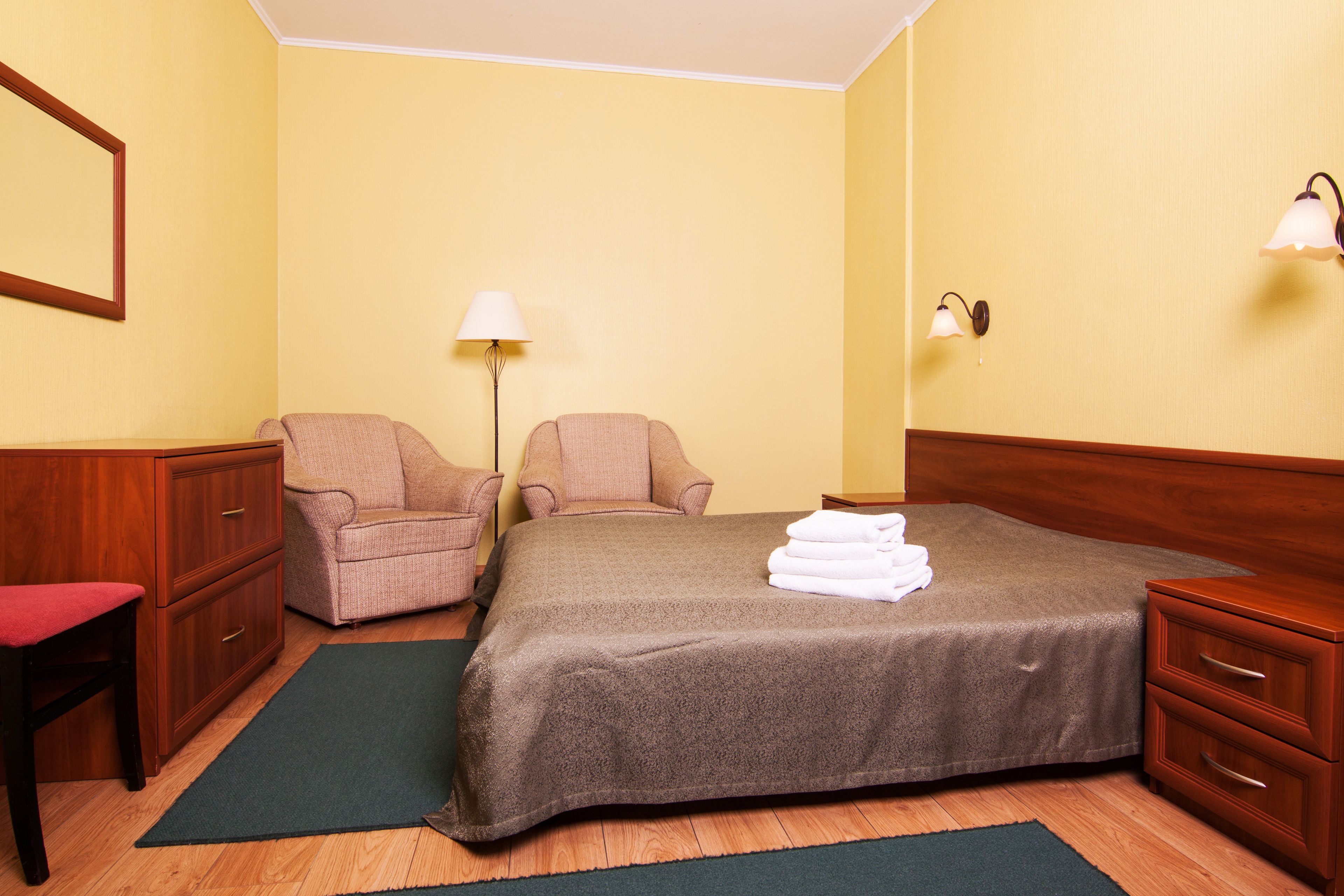 Una habitación de hotel con una cama, dos sillones, un escritorio y una lámpara.