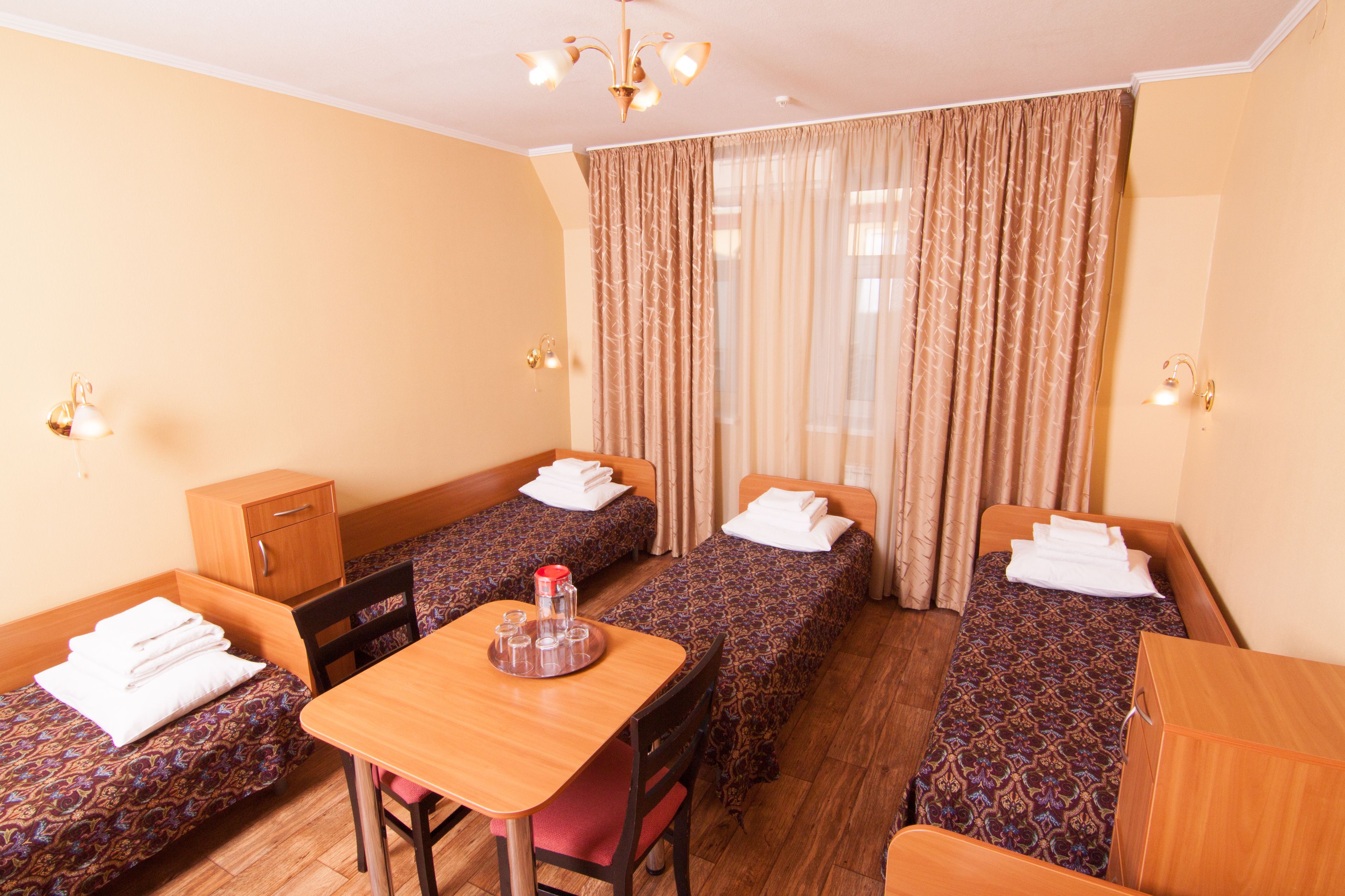 Habitación de hotel con dos camas individuales, una mesa de madera, una silla, un armario pequeño y una ventana con cortinas.