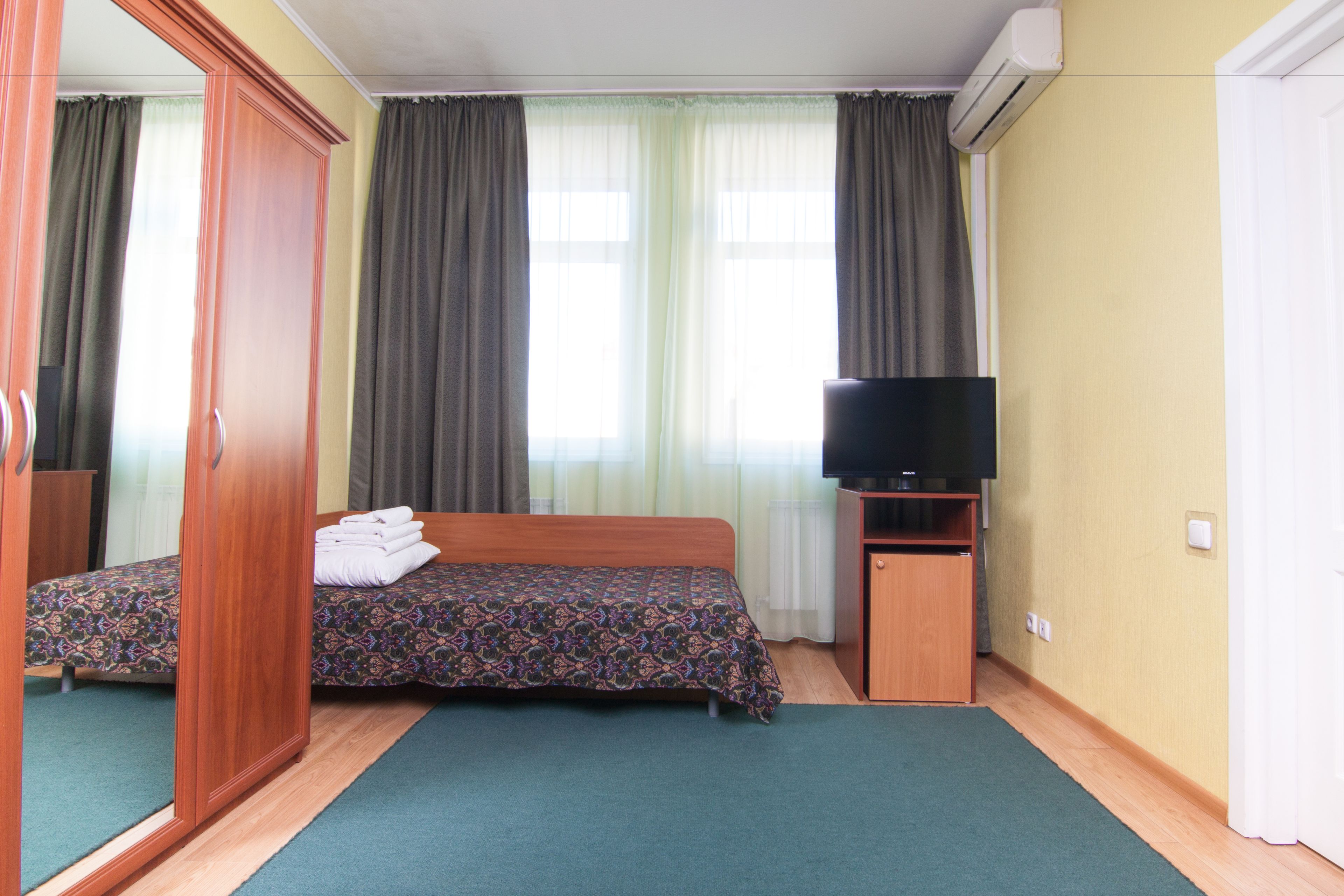 Une chambre d’hôtel avec un lit, une armoire, une télévision et une fenêtre avec des rideaux.