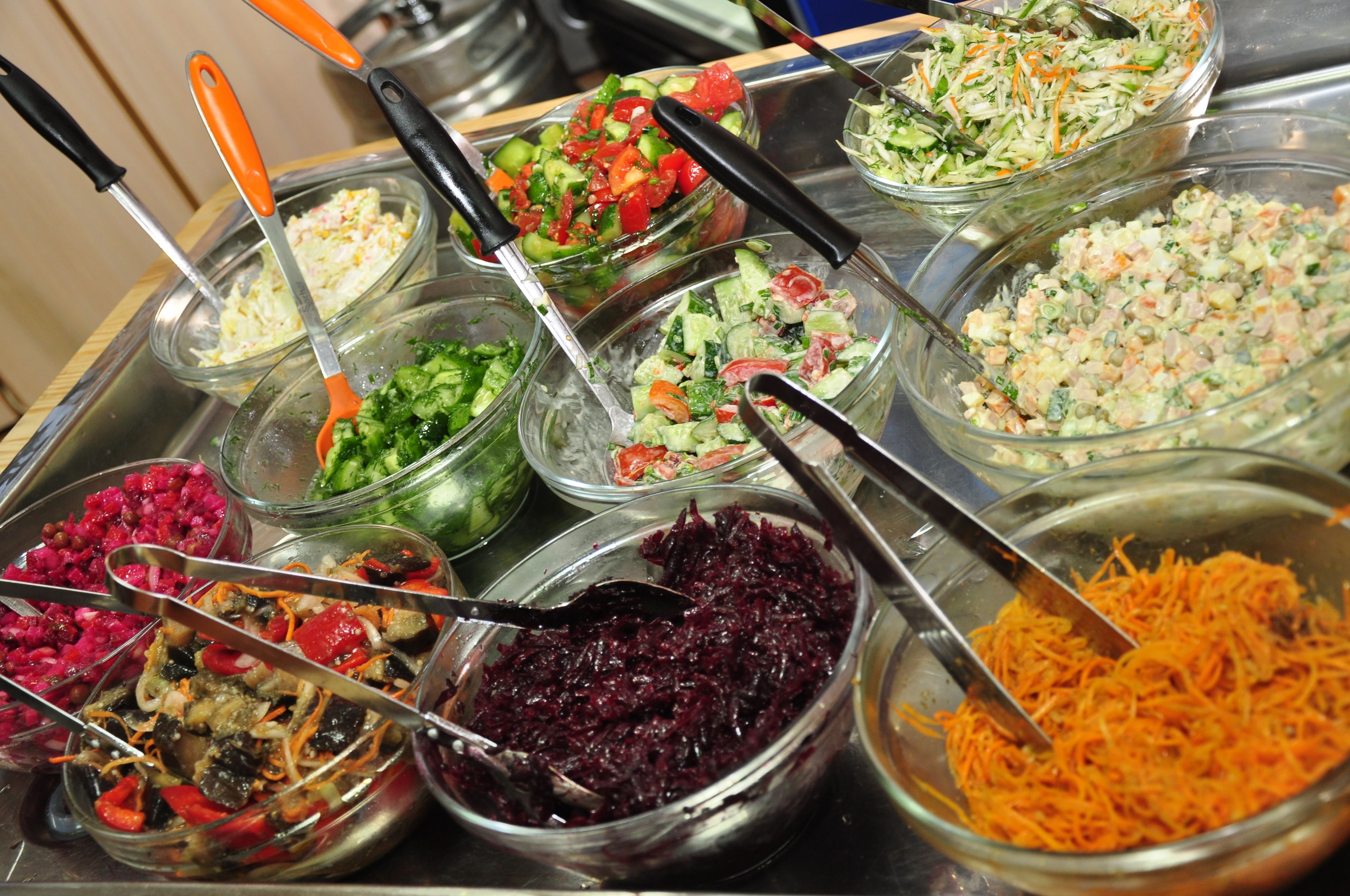 Un bufé con varios platos, incluyendo ensalada de col, ensaladas y verduras mixtas.