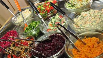 Un bufé con varios platos, incluyendo ensalada de col, ensaladas y verduras mixtas.