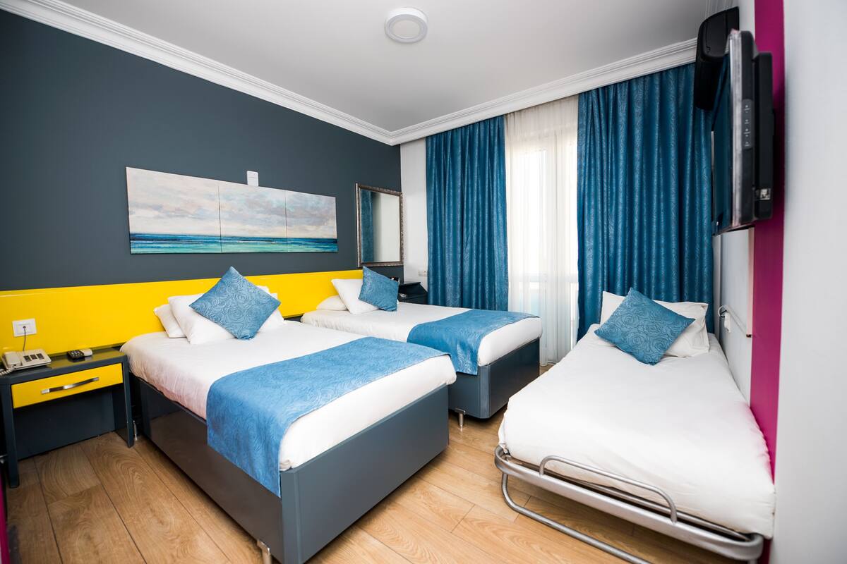 A hotel room with two beds, a nightstand, a desk, a mirror, and a painting on the wall.