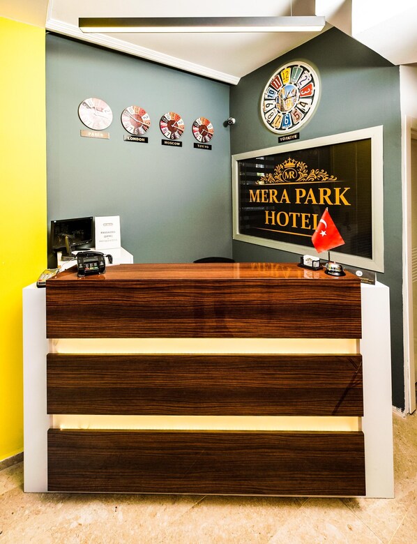 A reception desk with a clock, a sign for 'Mera Park Hotel,' and a flag.