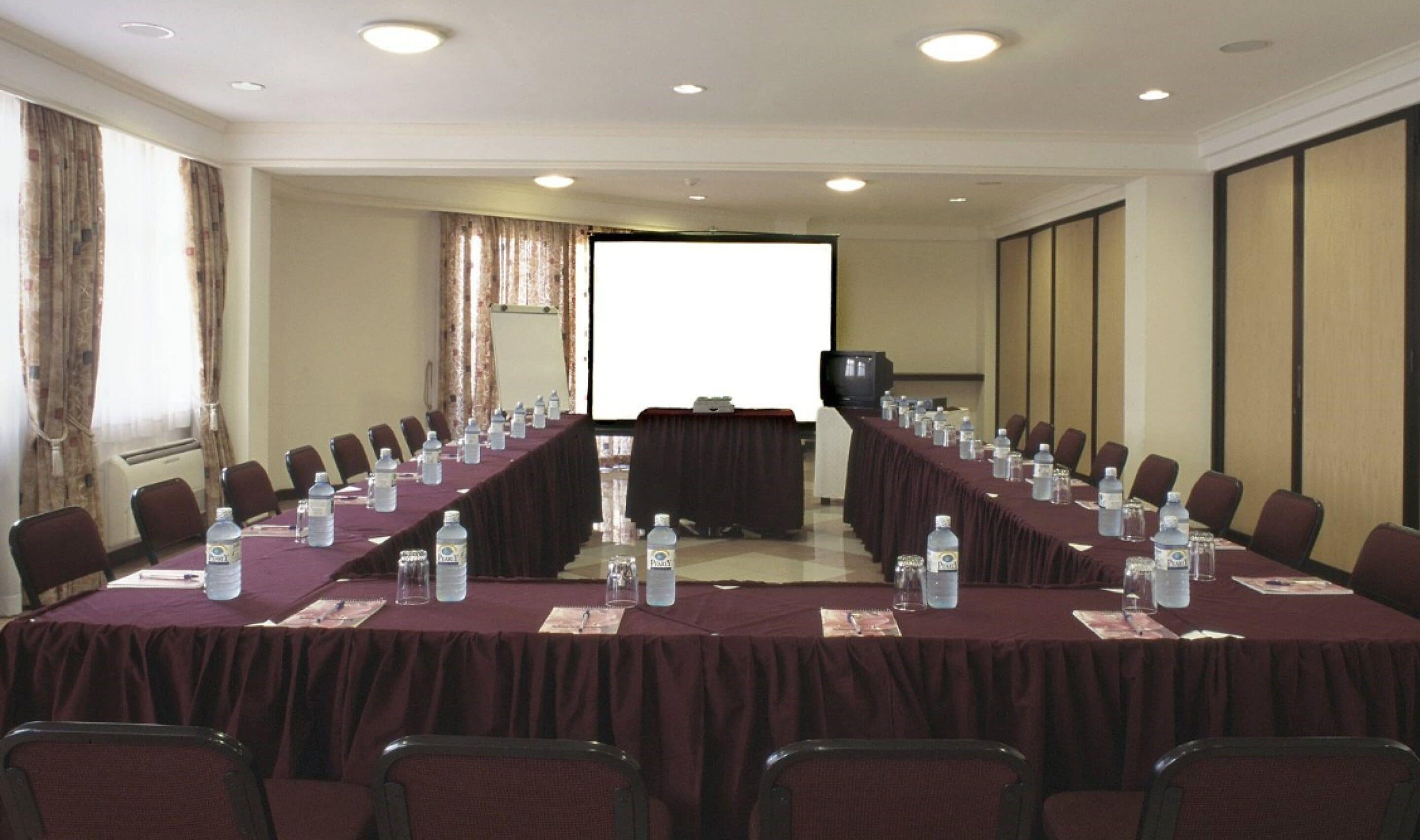 A conference room with a long table, chairs, water bottles, and a projector screen.